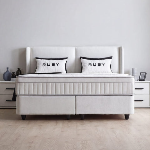 Ruby Boxspringbett in Velours Grau, Frontansicht mit Kopfteil, Matratze und Ruby-Kissen im hellen Schlafzimmer