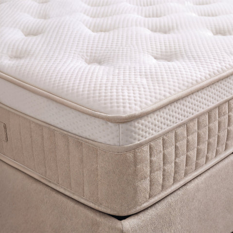 Nahaufnahme der Matratzenecke mit weisser Steppung auf beigem Boxspringbett Unterbau