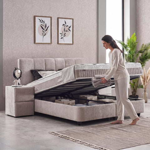 Geöffneter Bettkasten des Lucia Boxspringbetts in Grau-Beige, Frau hebt Liegefläche an, viel Stauraum unter Matratze und Topper