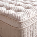 Nahaufnahme der gesteppten Topper Oberfläche und beiger Bouclé Verkleidung des Boxspringbetts