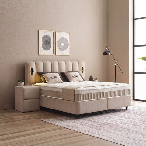 Wind Boxspringbett in Beige, seitliche Ansicht mit Stoffbezug, Kopfteil und Nachttisch im hellen Schlafzimmer