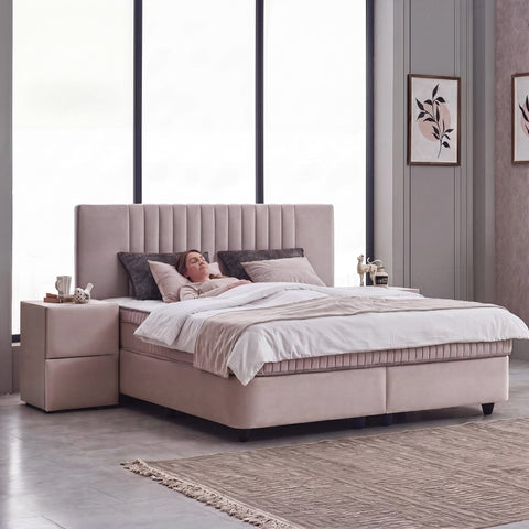Frau liegt auf dem Clara Boxspringbett aus Samt in Braun-Beige, seitliche Schlafzimmer-Szene zeigt Liegekomfort und Nachttisch