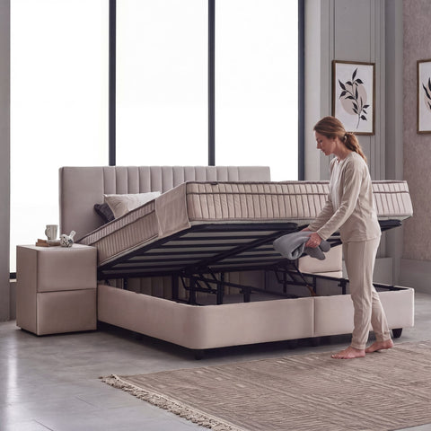 Clara Boxspringbett Samt Braun-Beige mit geöffnetem Bettkasten, Frau hebt Liegefläche an und zeigt praktischen Stauraum