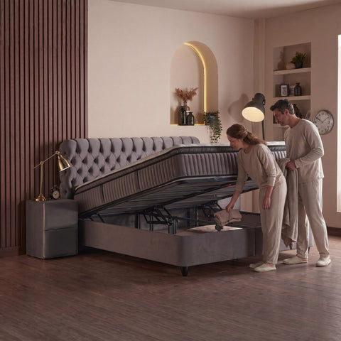 Sydney Boxspringbett Samt Grau mit geöffnetem Bettkasten, Paar nutzt Stauraum unter der hochgeklappten Liegefläche